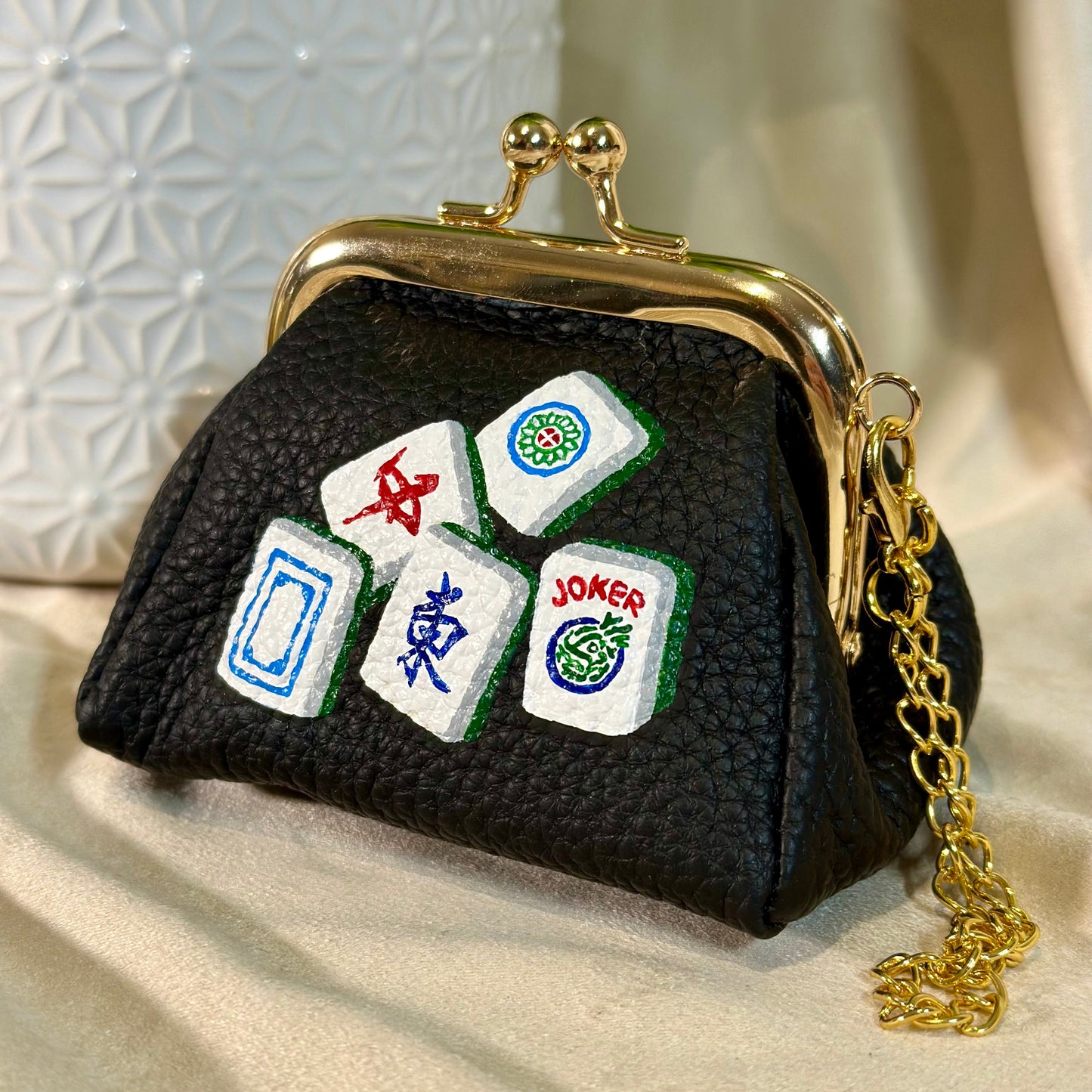 Black purse with Mahjong tile designs on a beige surface