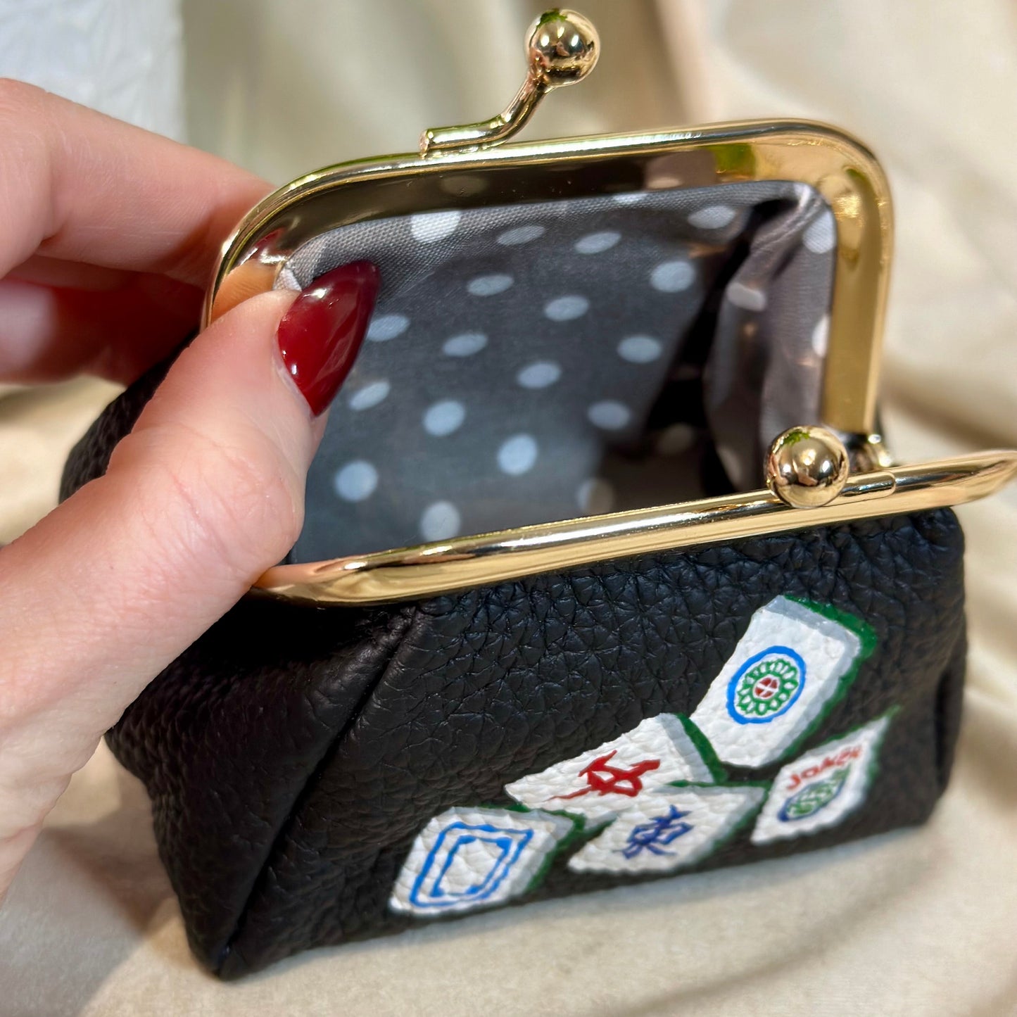 Black pouch with embroidered dice designs held by a hand against a neutral background