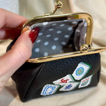 Black pouch with embroidered dice designs held by a hand against a neutral background