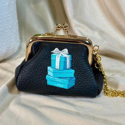 Black handbag with blue gift box design on a beige fabric background