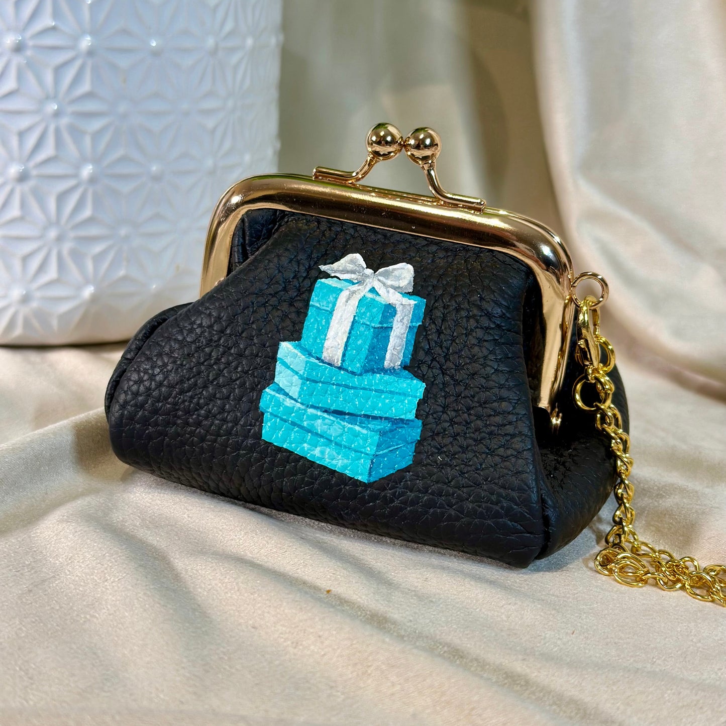 Black purse with gold clasp and blue gift box design on a beige surface