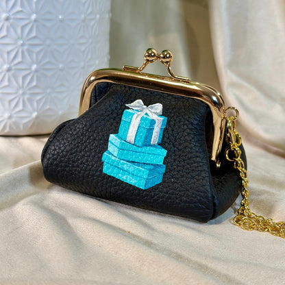 Black purse with gold clasp and blue gift box design on a beige surface