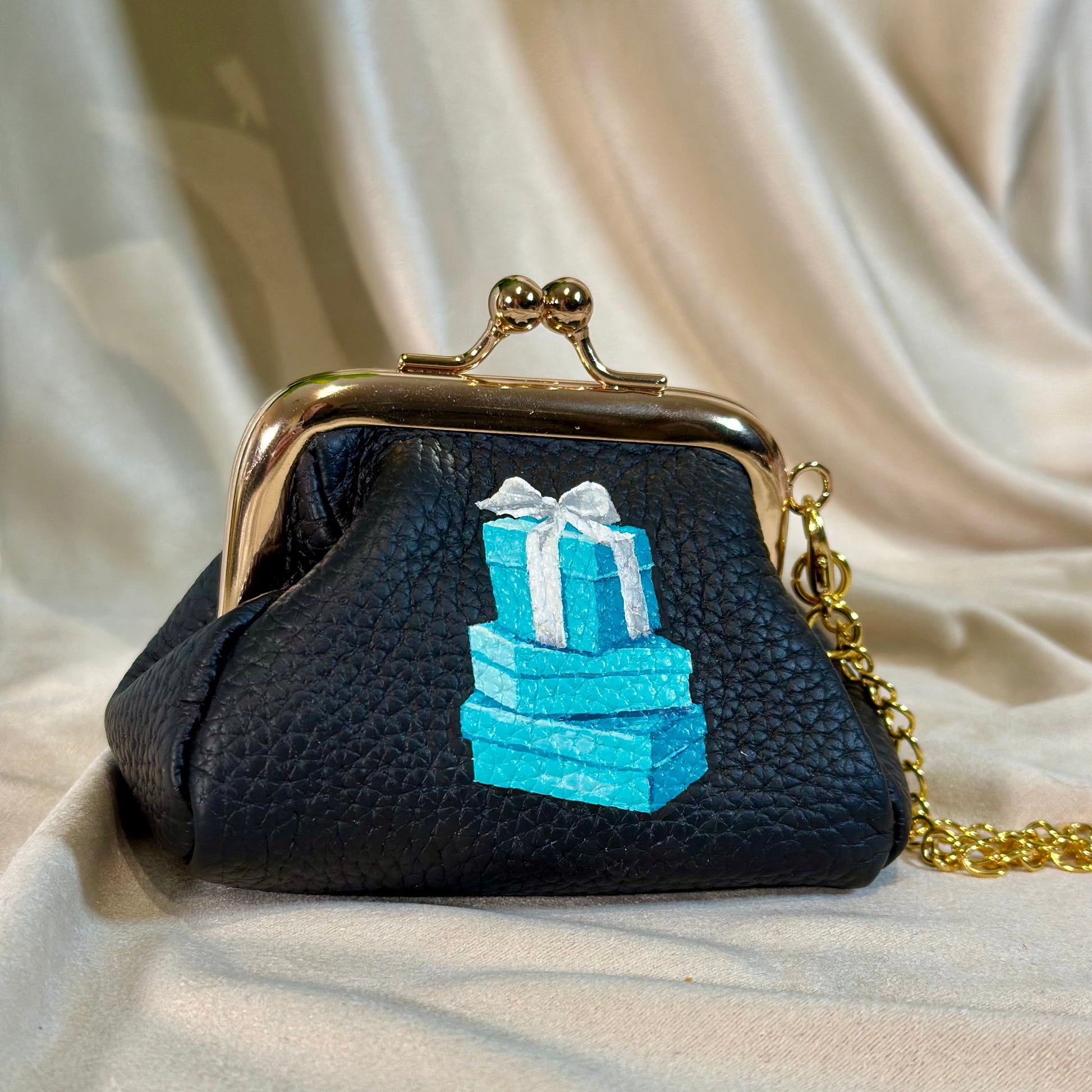 Black handbag with blue gift box design on a beige fabric background