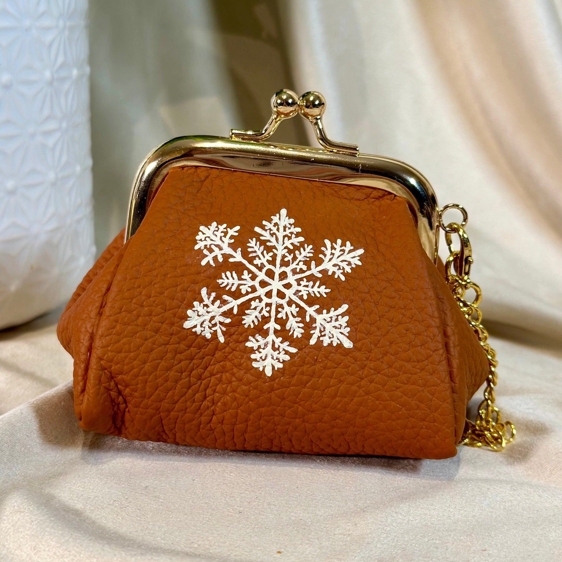 Brown purse with gold clasp and white snowflake design on a light background
