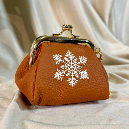 Brown leather purse with a white snowflake design on a beige fabric background