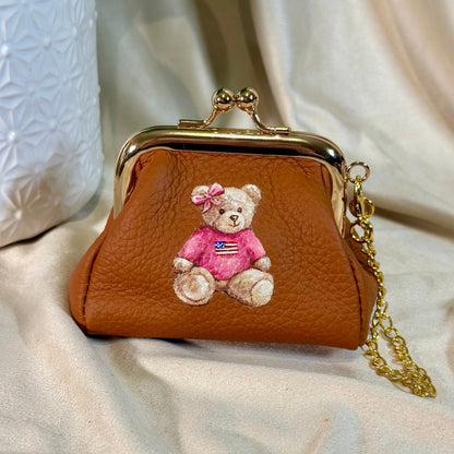 Brown leather purse with teddy bear design on a beige fabric background