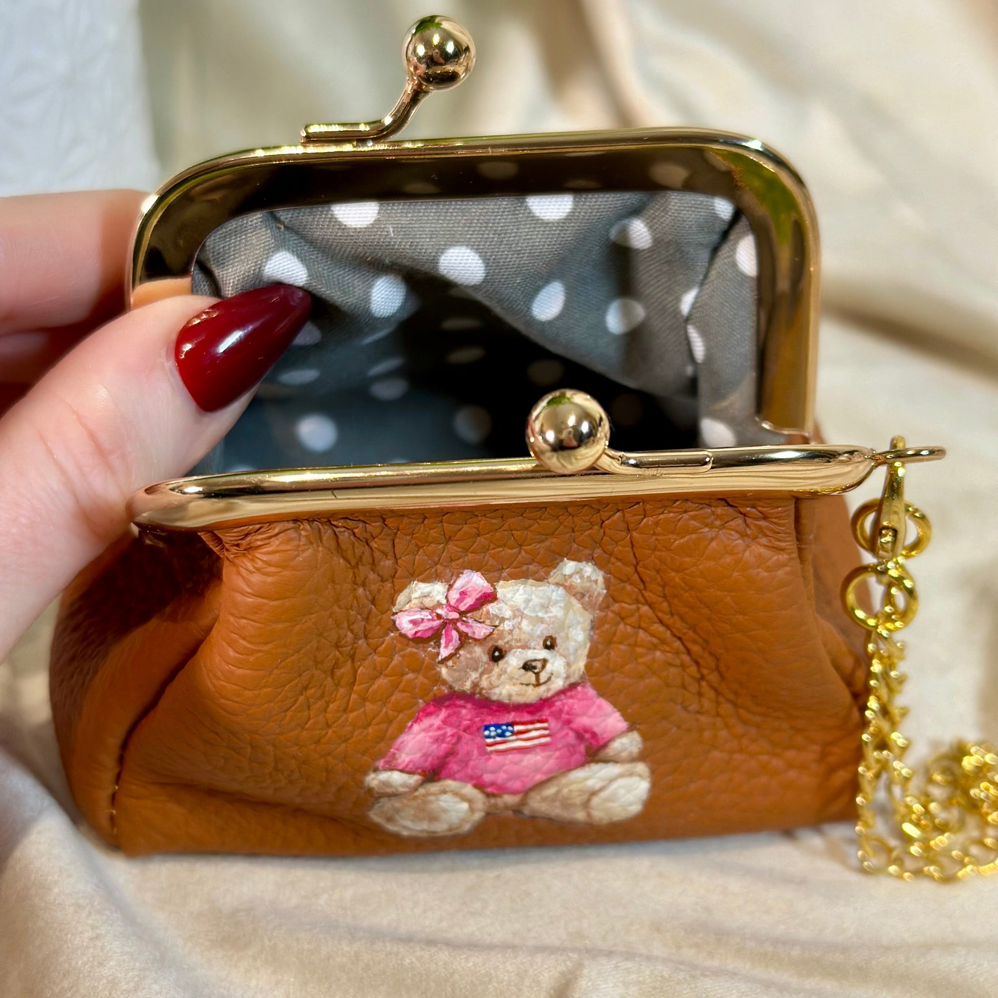 Brown purse with teddy bear design held by a hand on a beige background