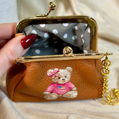 Brown purse with teddy bear design held by a hand on a beige background