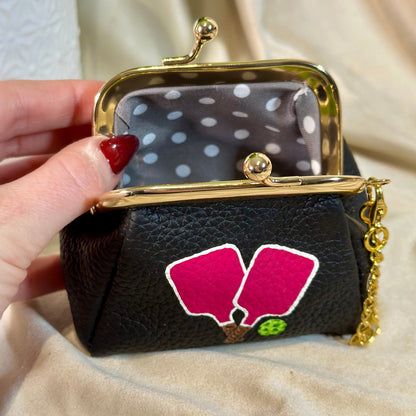 Black pouch with pink floral design held by a hand against a beige background