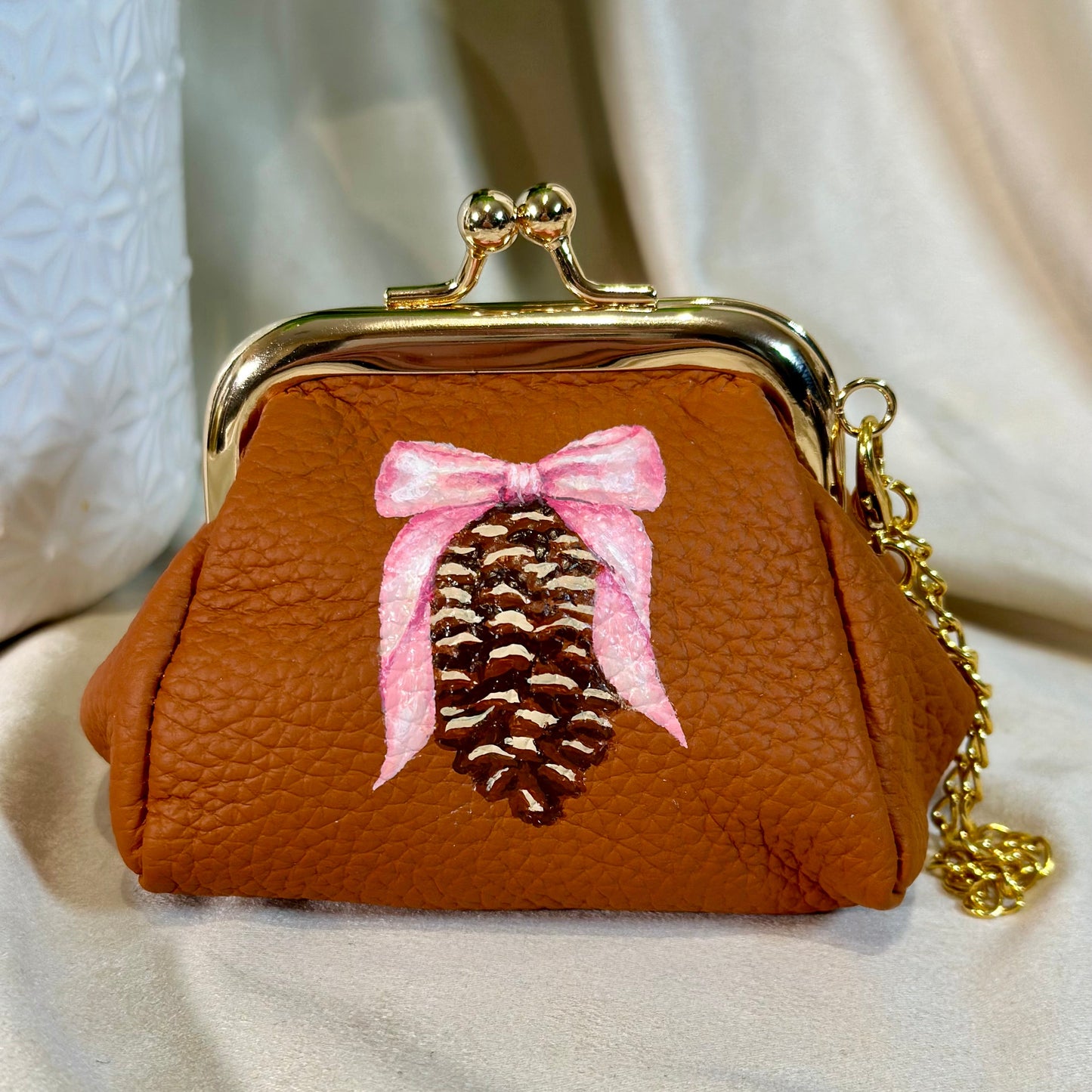 Brown purse with a pine cone and pink bow design on a light background