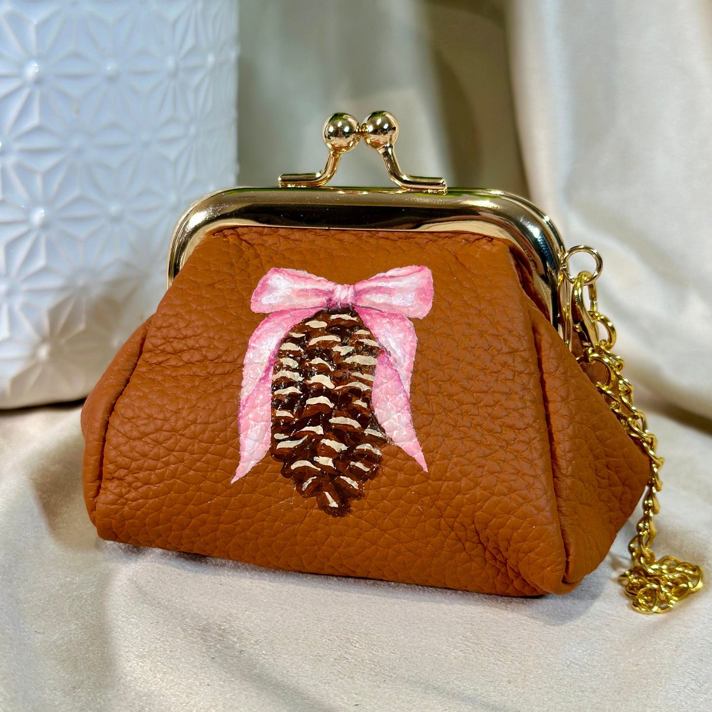 Brown purse with a pine cone and pink bow design on a light background