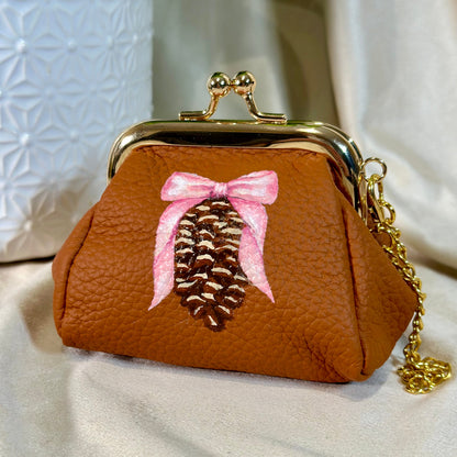 Brown purse with a pine cone and pink bow design on a light background
