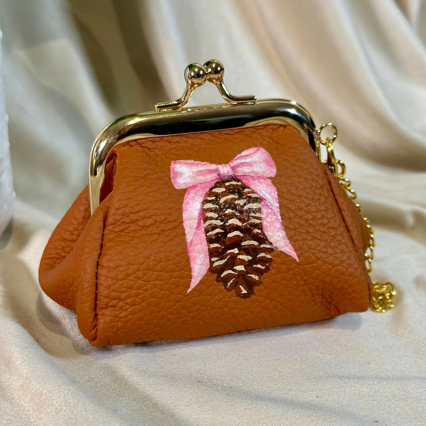 Small brown purse with a pine cone and pink bow design on a beige fabric background