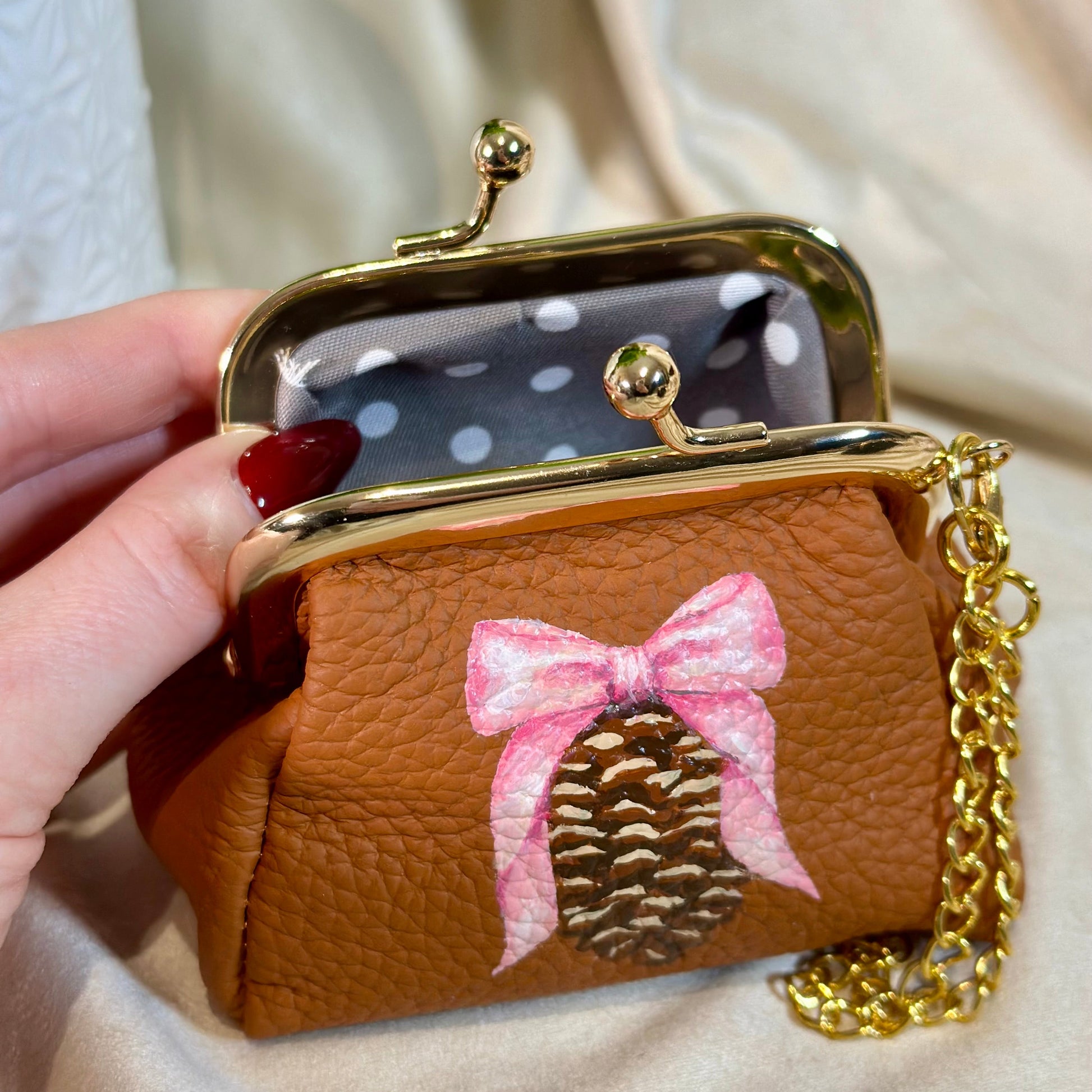 Small brown purse with a pink bow and gold chain held by a hand.