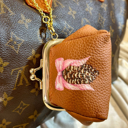 Brown leather pouch with floral design in front of a patterned handbag