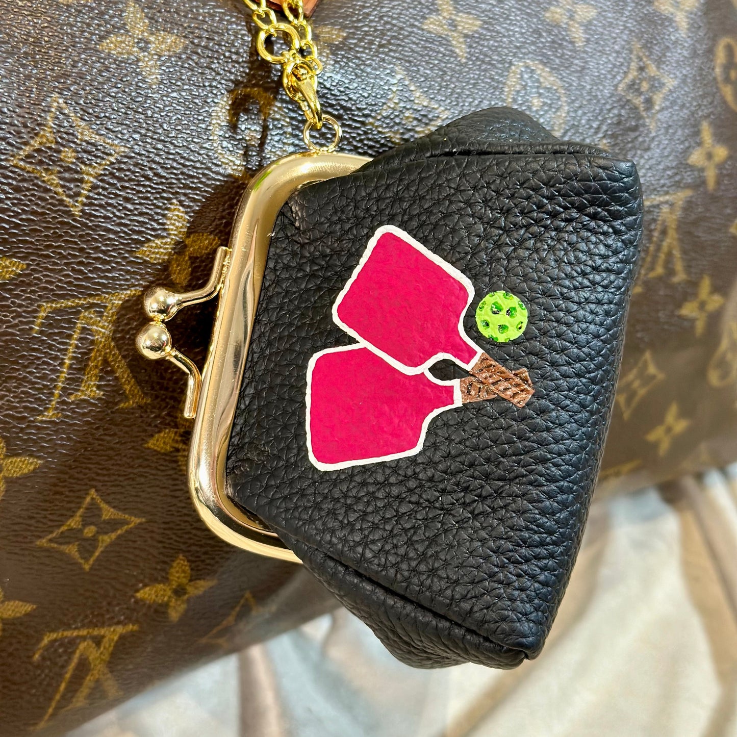 Black coin purse with pink and green design on a brown patterned bag