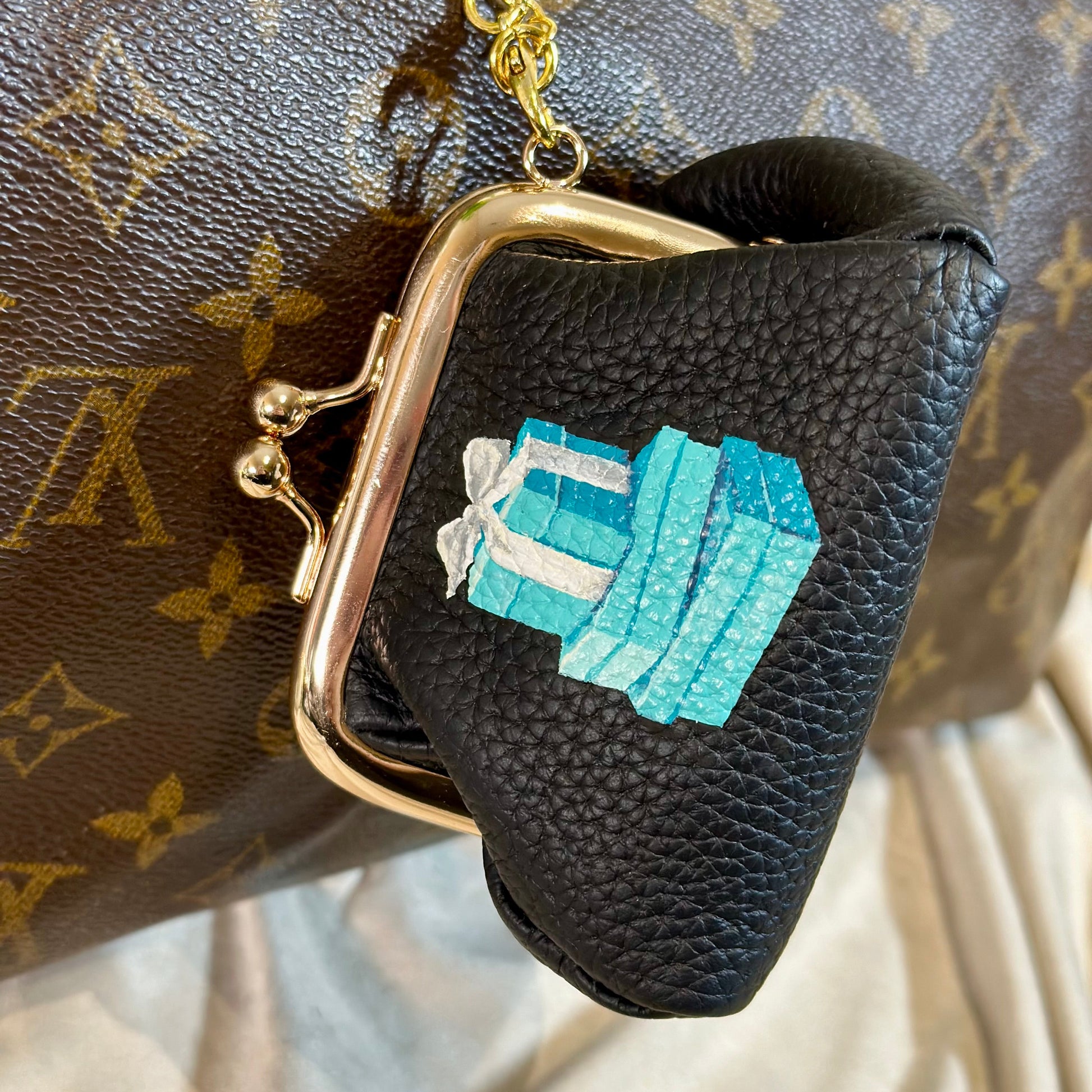 Black leather pouch with gold clasp and blue gemstone design on a patterned background