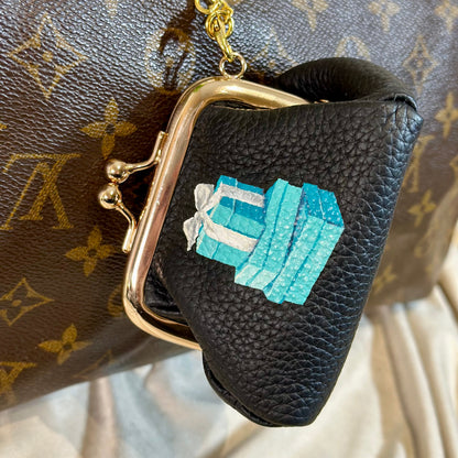 Black leather pouch with gold clasp and blue gemstone design on a patterned background