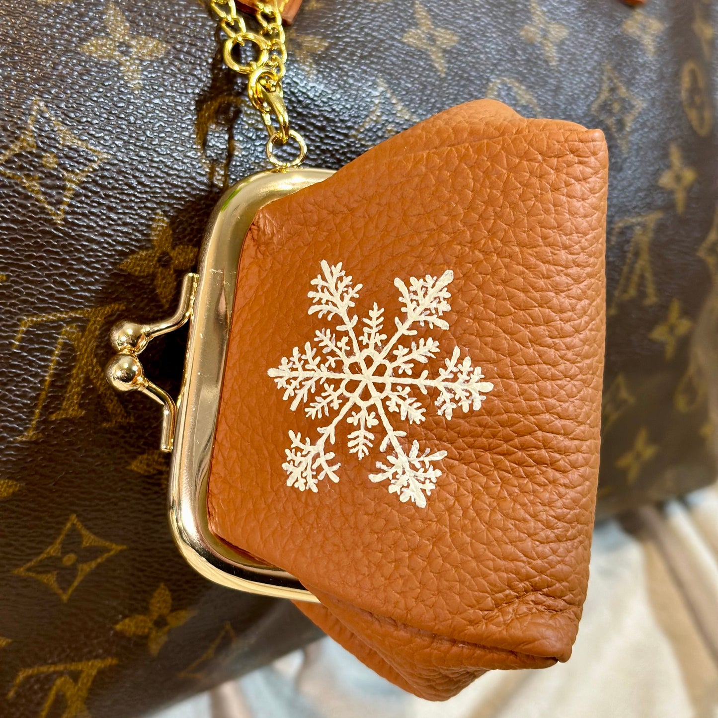 Brown leather pouch with gold clasp and snowflake design on a patterned background