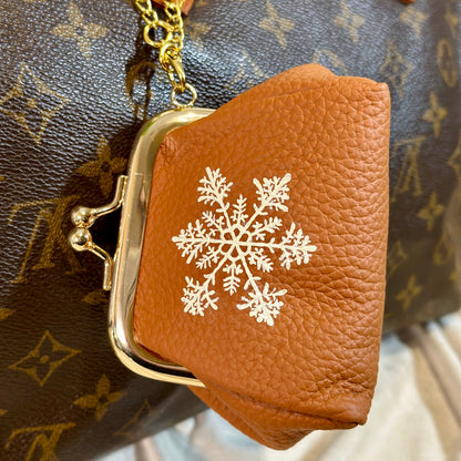 Brown leather pouch with gold clasp and snowflake design on a patterned background