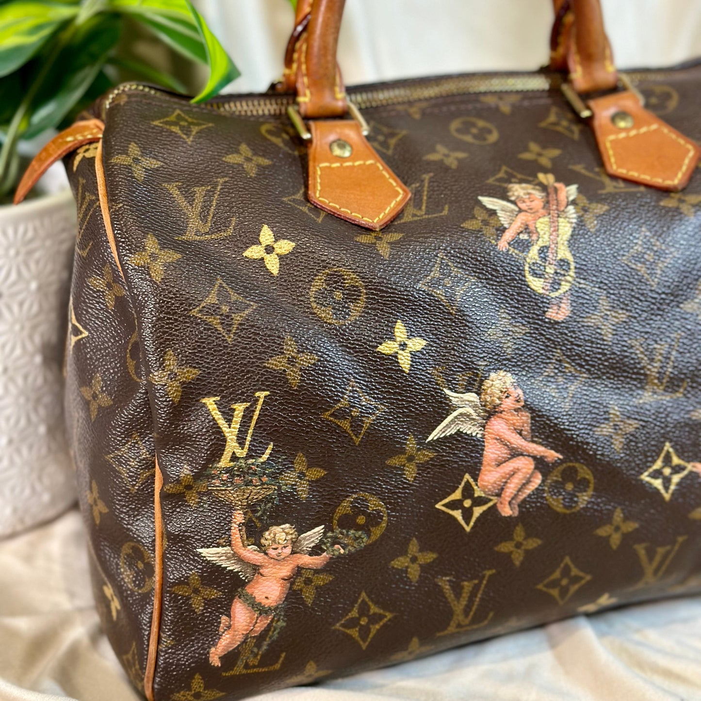 Designer handbag with monogram pattern and cherub designs on a neutral background