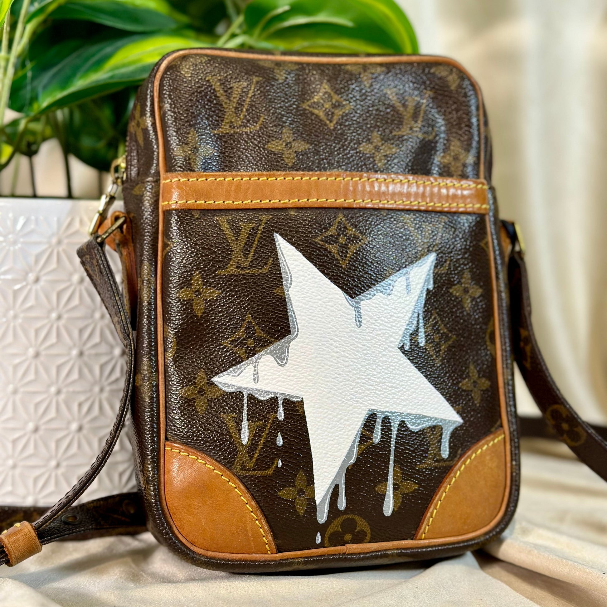 Designer handbag with a white star and brown monogram pattern on a light surface.