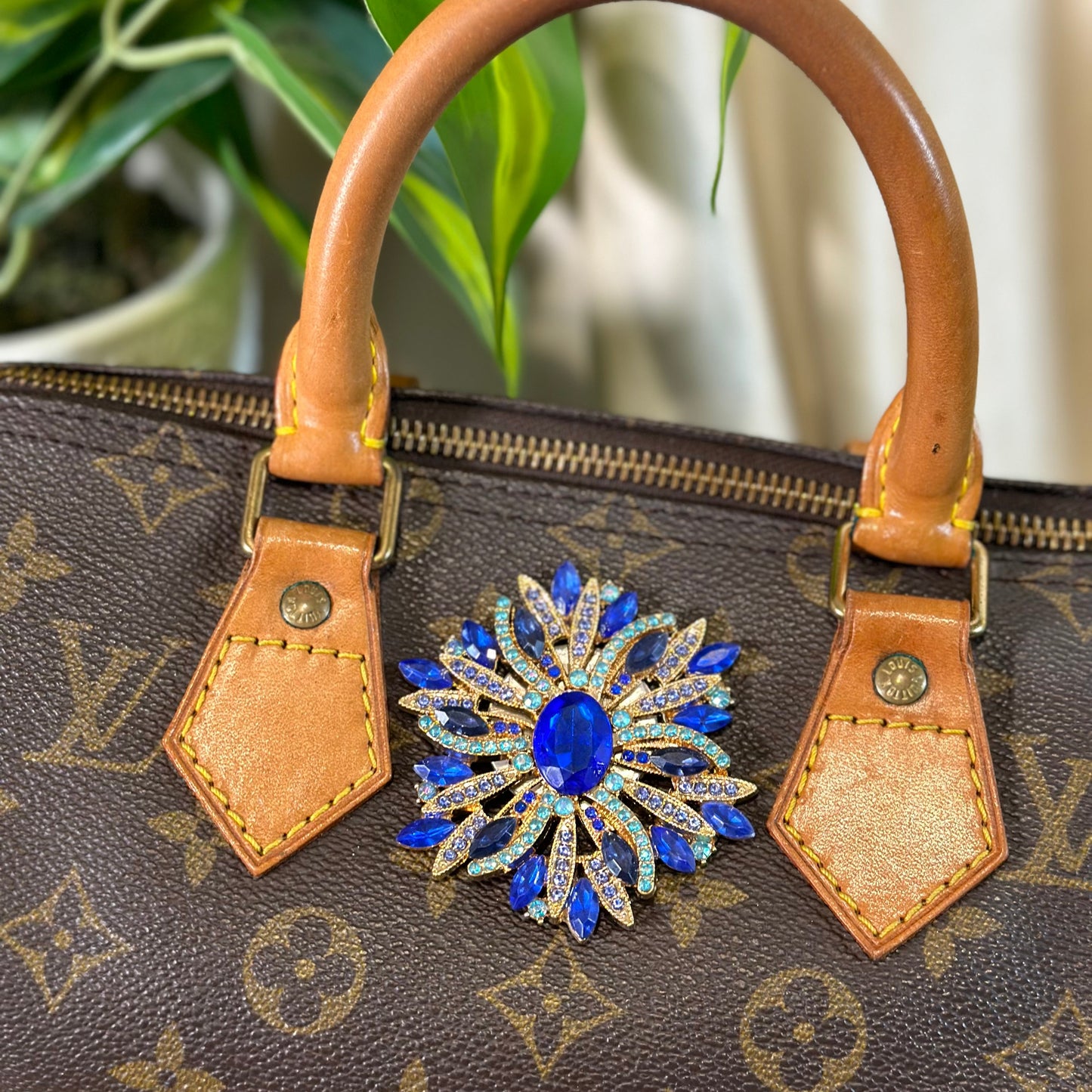 Brown handbag with a decorative blue brooch on a blurred background