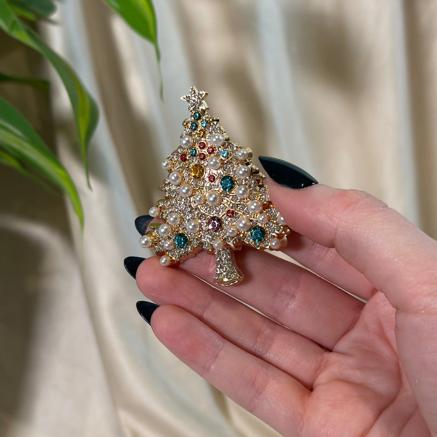 Hand holding a decorative brooch with gemstones against a neutral background