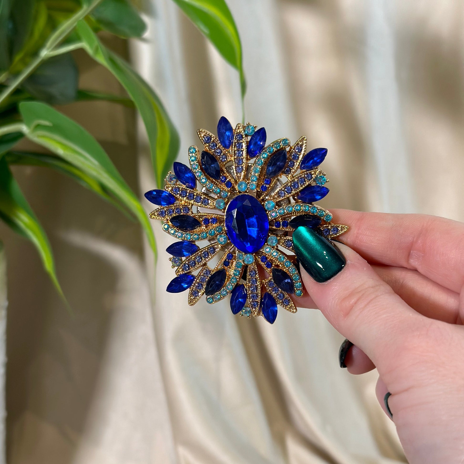 Hand holding a decorative brooch with blue and gold details against a neutral background