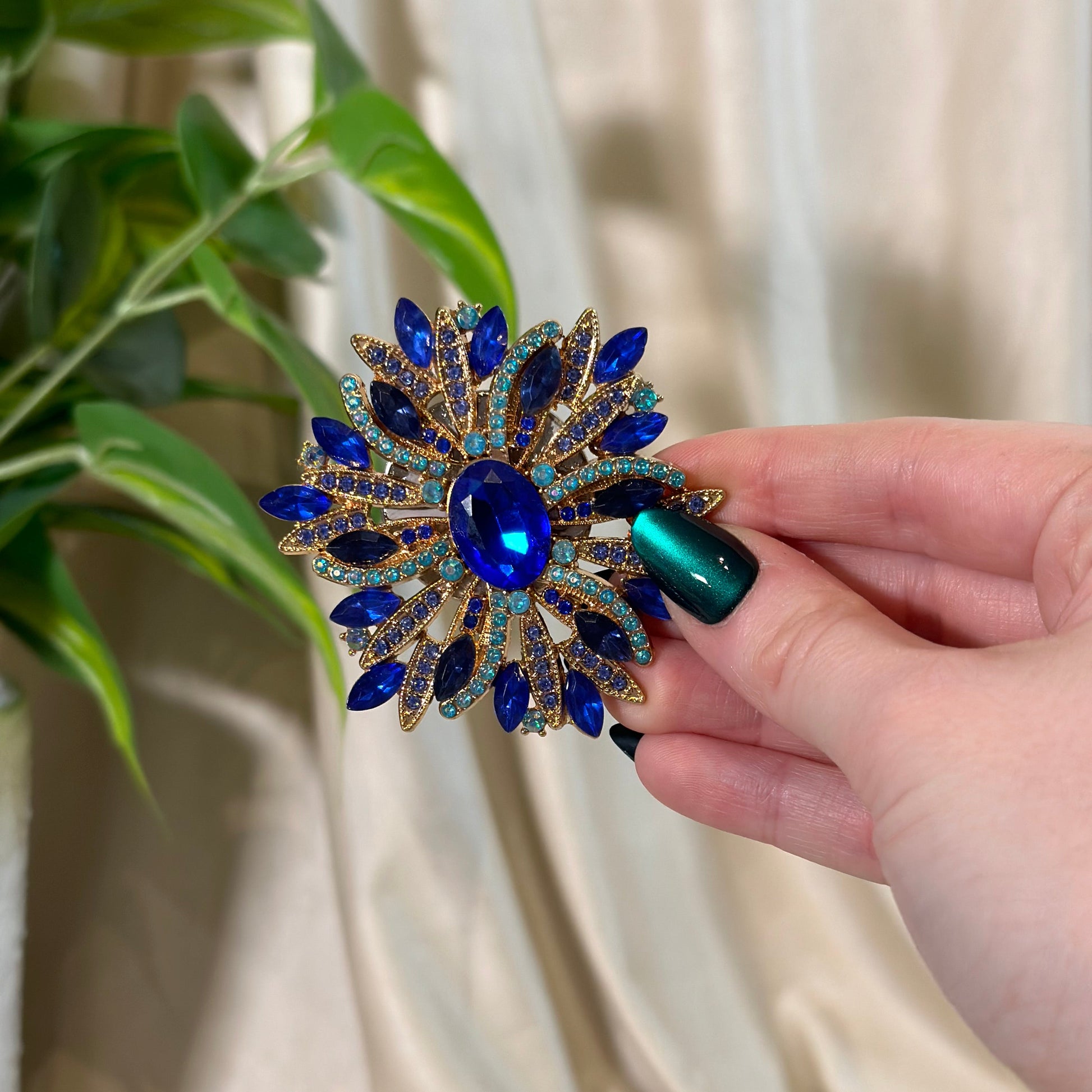 Hand holding a decorative brooch with blue gemstones against a neutral background