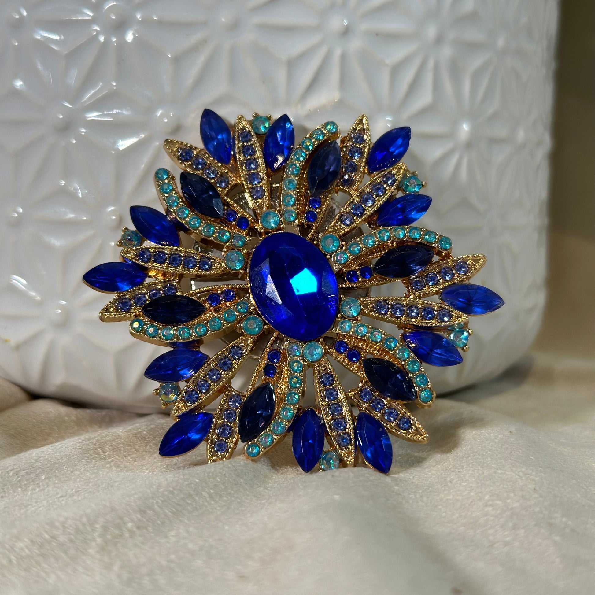 Decorative brooch with blue gemstones and gold accents on a textured white surface