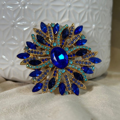 Decorative brooch with blue gemstones and gold accents on a textured white surface