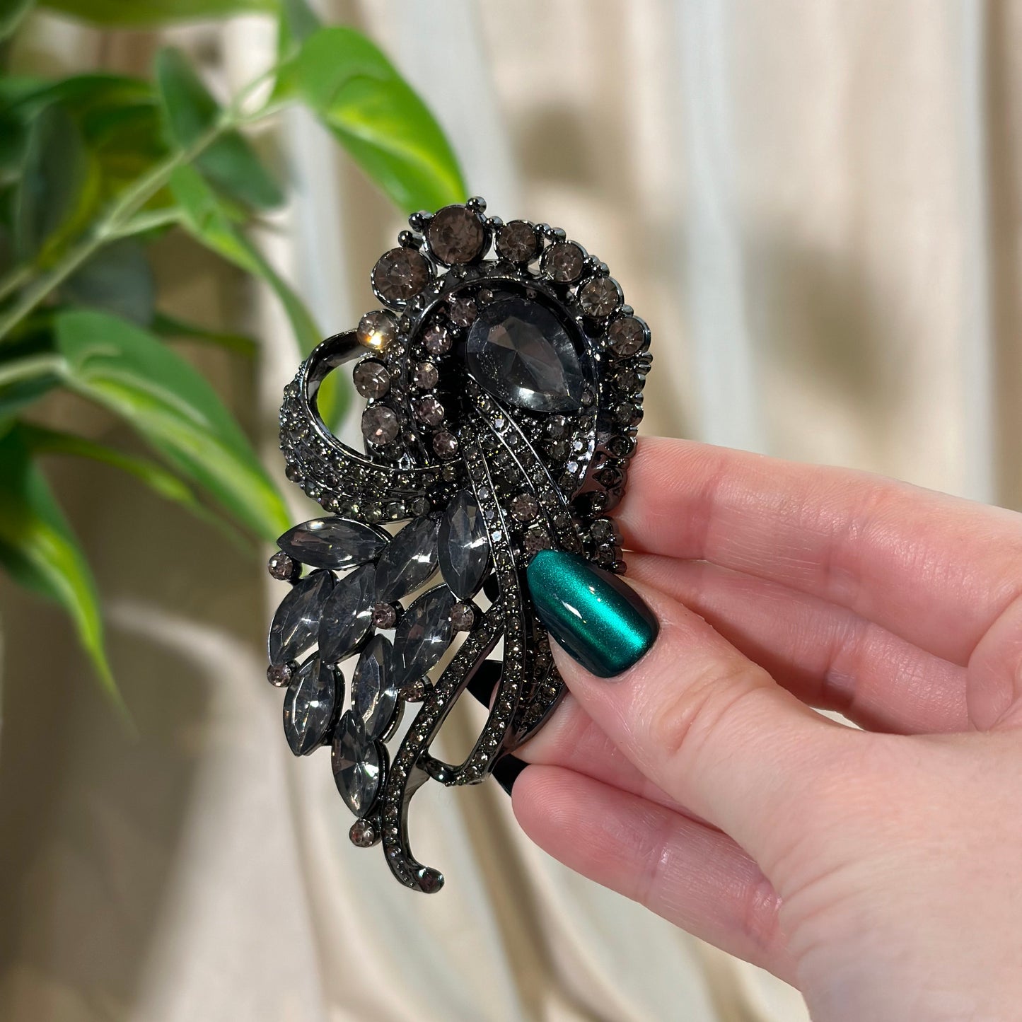 Hand holding a decorative black spider brooch with green nail polish against a neutral background