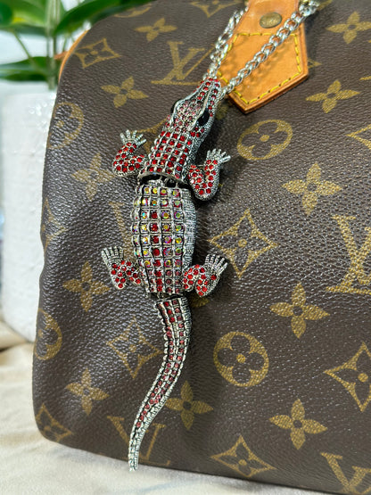Decorative lizard charm on a Louis Vuitton handbag with monogram pattern.