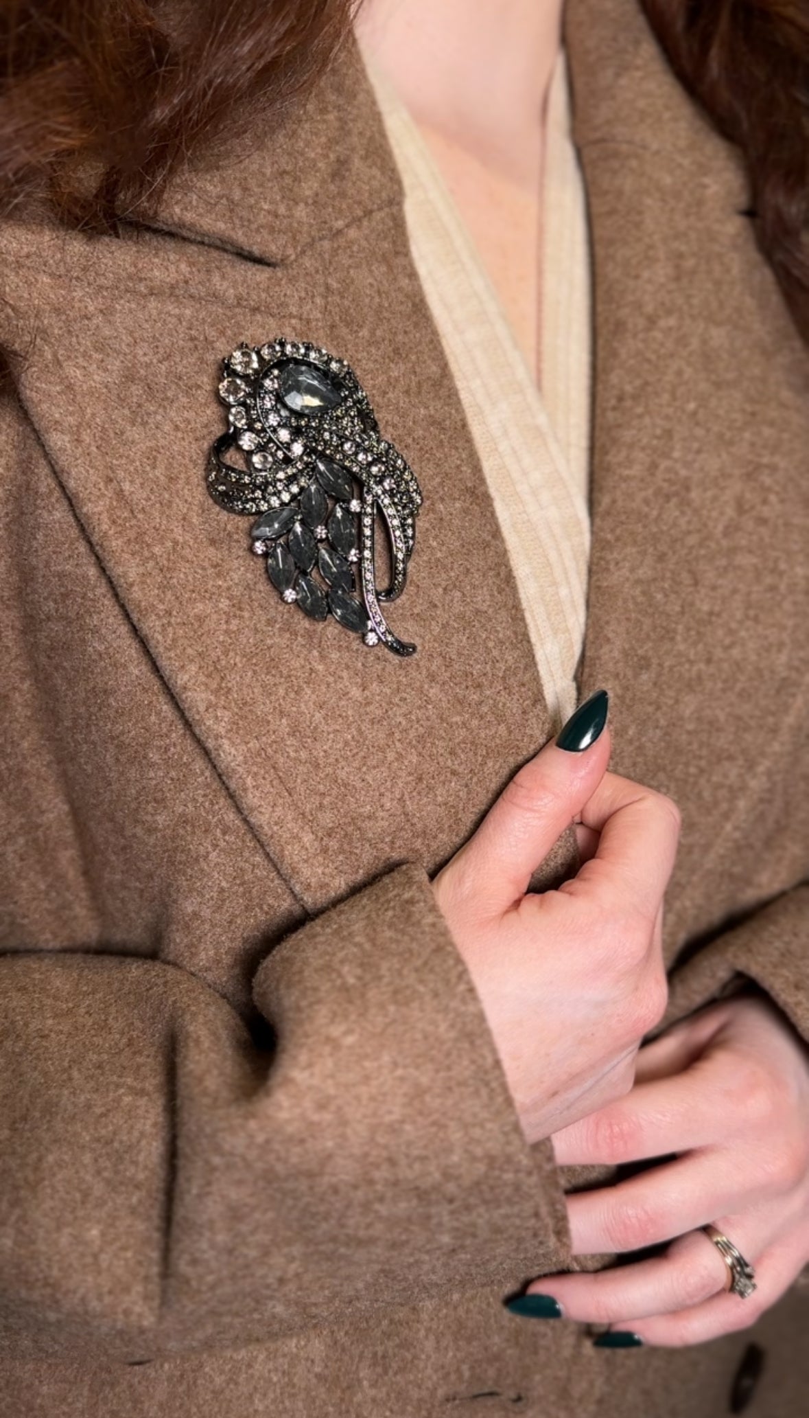 Close-up of a person wearing a brown coat with a decorative brooch and a hand adjusting the collar.