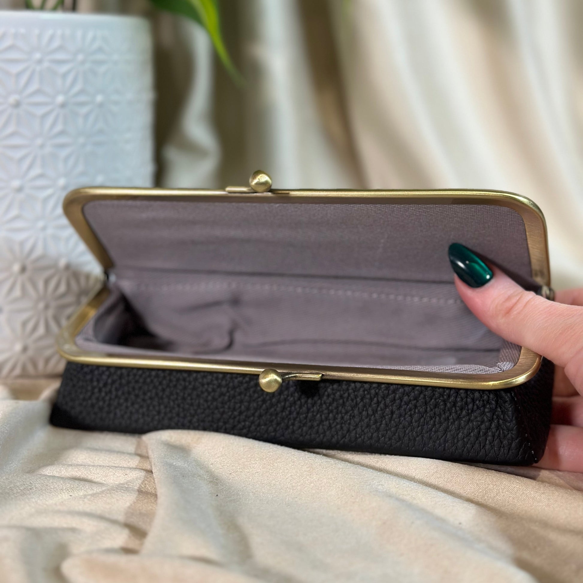 Black clutch with gold frame held by a hand against a neutral background