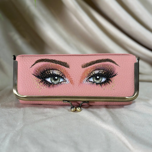 Pink clutch with eye makeup design on a beige fabric background
