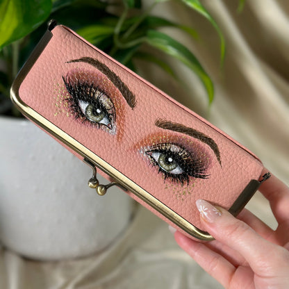 Hand holding a pink wallet with eye design against a neutral background