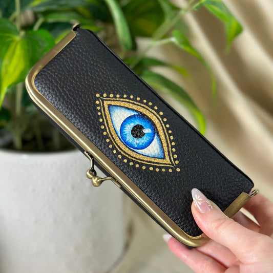 Black wallet with eye design held by a hand in front of a plant