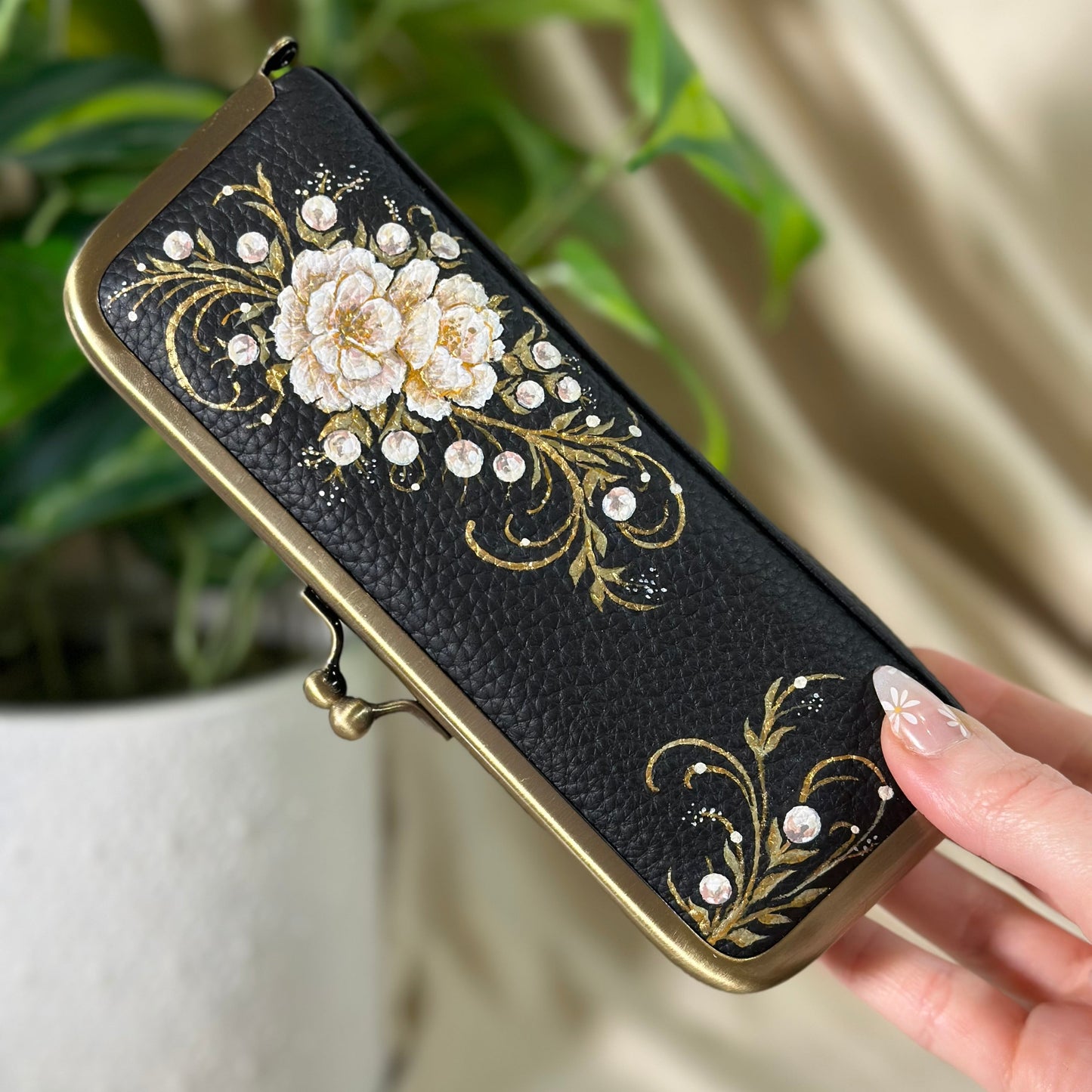 Decorative black wallet with floral embroidery held by a hand, with a plant in the background.