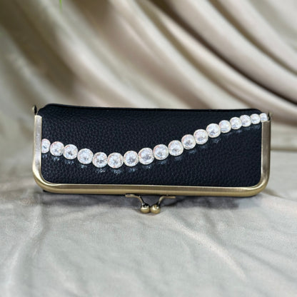Black clutch with pearl embellishments on a beige fabric background
