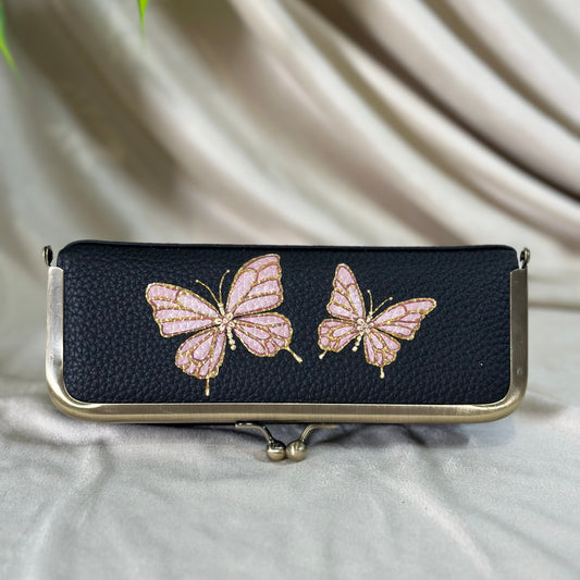 Black clutch with pink butterfly designs on a beige fabric background