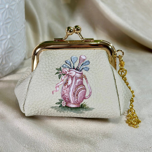 Small cream-colored purse with a pink golf bag design on a beige surface