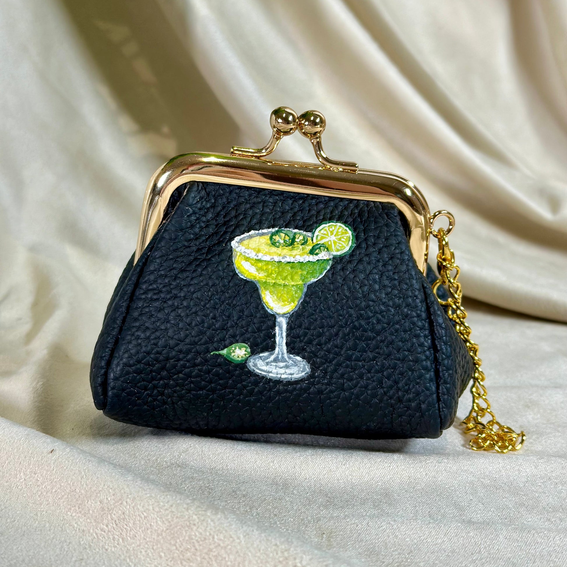 Black purse with a gold chain and a design of a cocktail on a beige fabric background