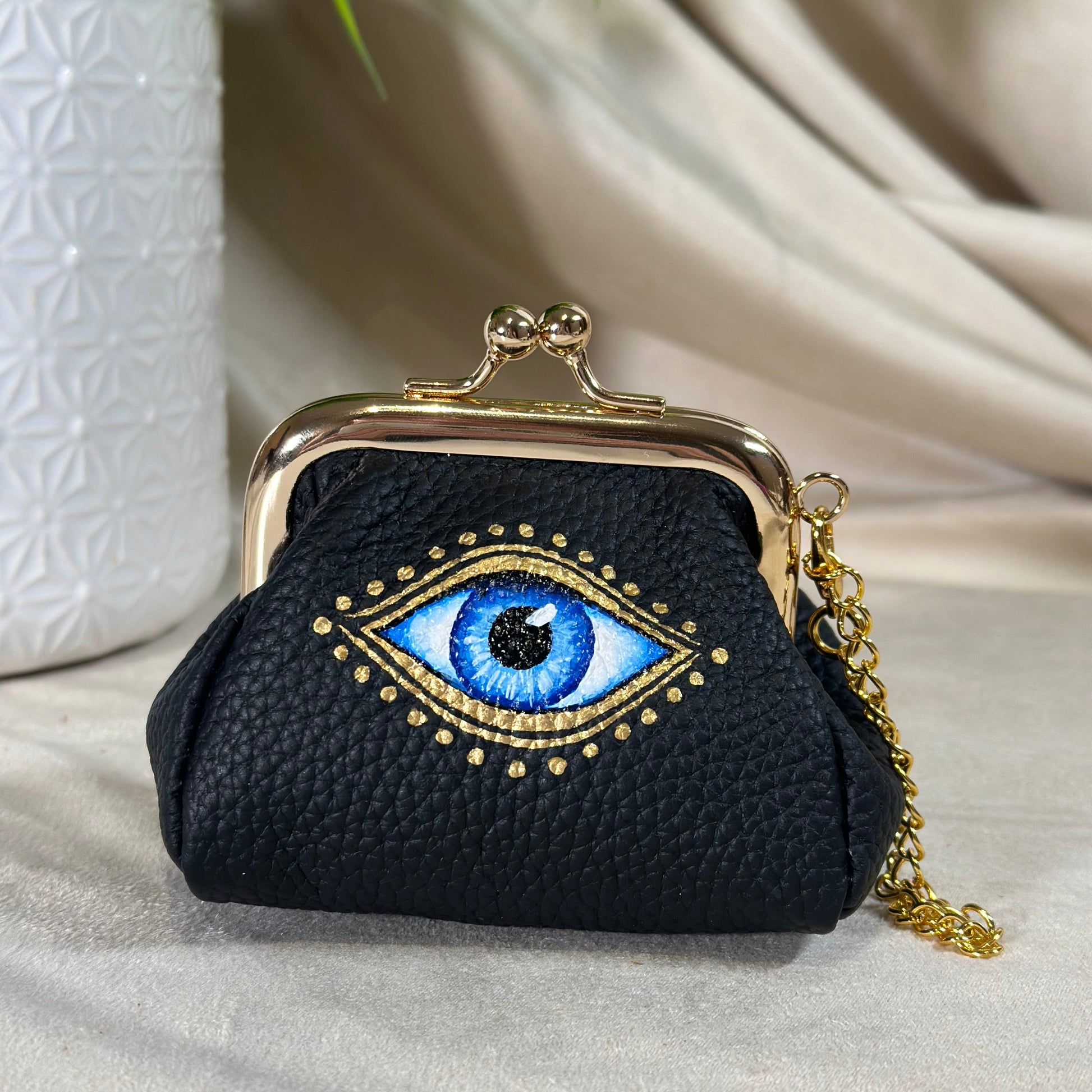 Black handbag with an embroidered eye design on a neutral background