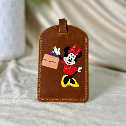 Brown leather luggage tag with cartoon character holding a Louis Vuitton tag on a light background