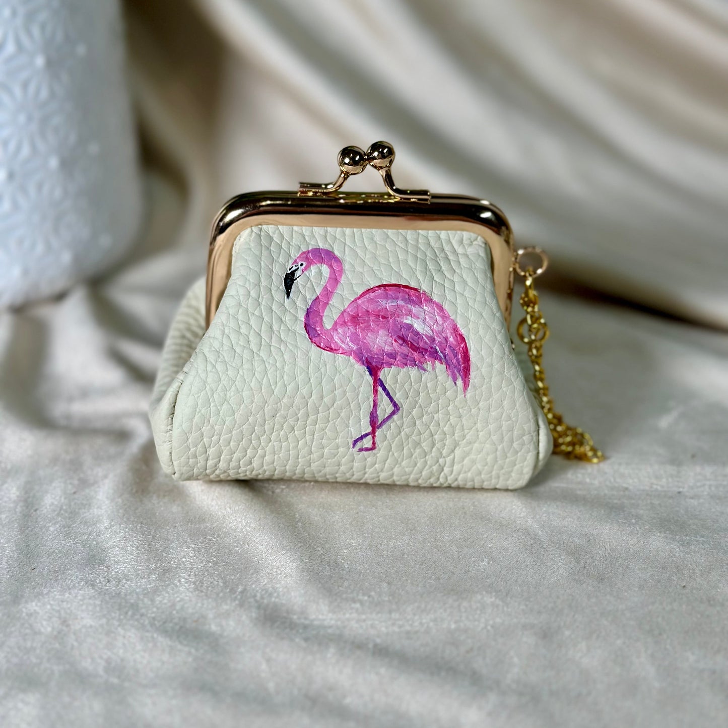 Small white purse with a pink flamingo design on a light fabric background