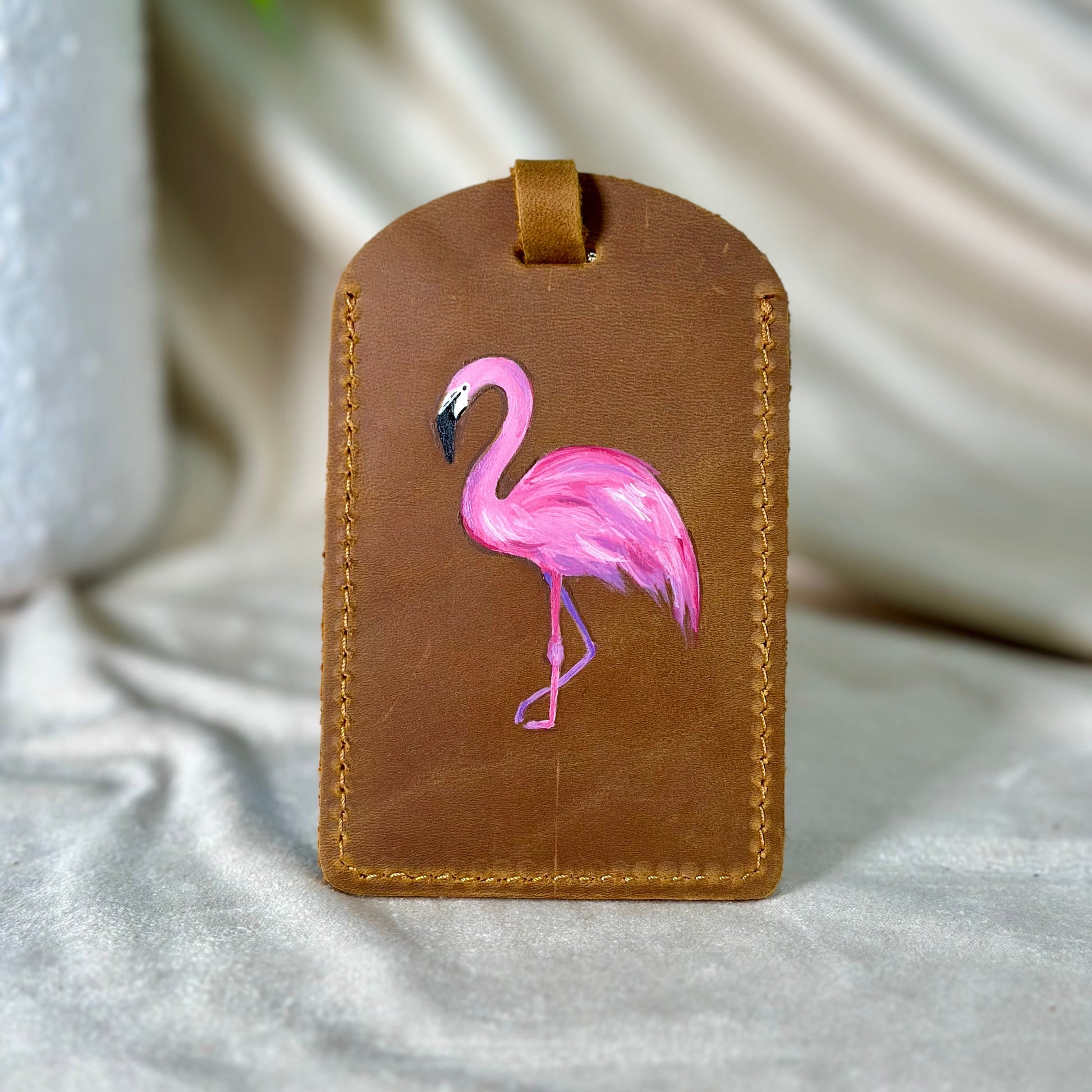 Brown leather luggage tag with a pink flamingo design on a light fabric background