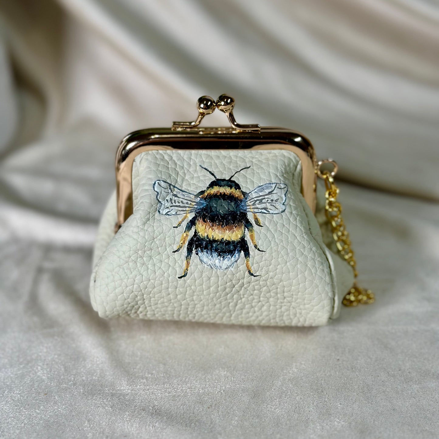 Small white purse with bee design on a light fabric background