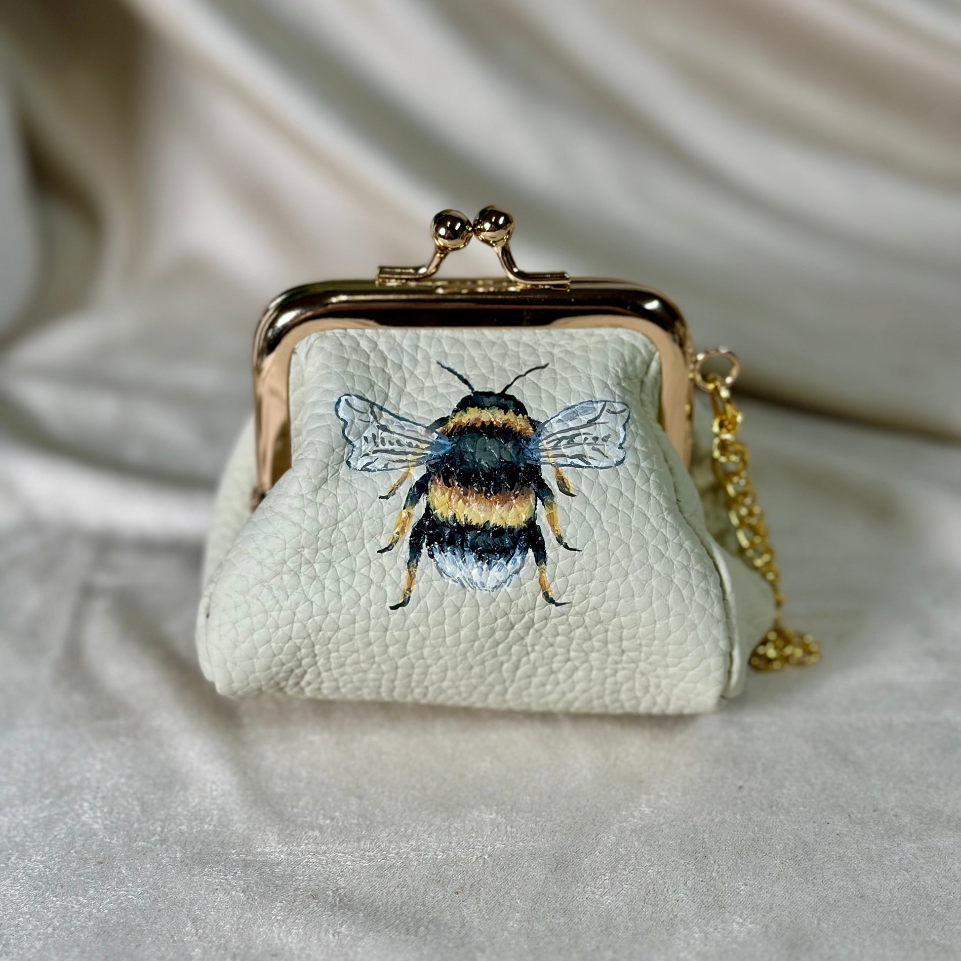 Small white purse with bee design on a light fabric background